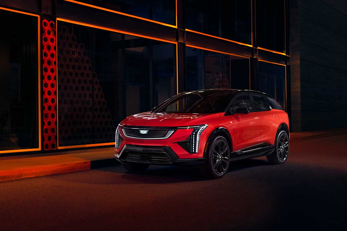 Red 2026 Cadillac OPTIQ parked at night beside a modern building, illuminated by signature vertical LED lights and bold exterior styling.