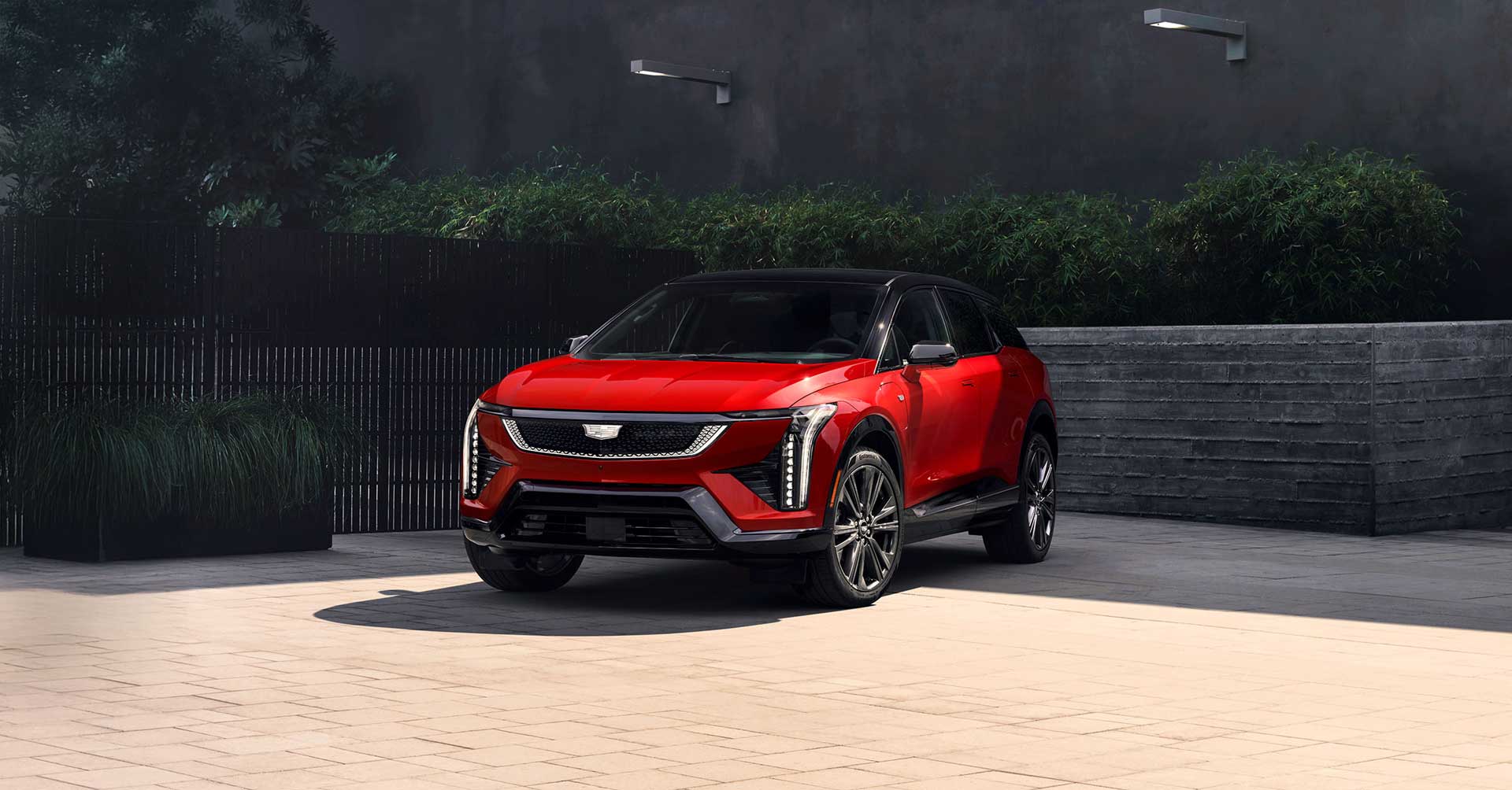 Red 2026 Cadillac OPTIQ with black roof and signature vertical LED headlights parked in a modern outdoor setting.