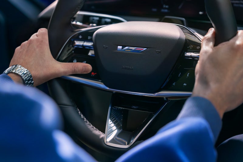 Close-up of a Man About to Press the V-Button on the 2026 OPTIQ-V Steering Wheel | Fitzgerald Cadillac Annapolis in Annapolis MD