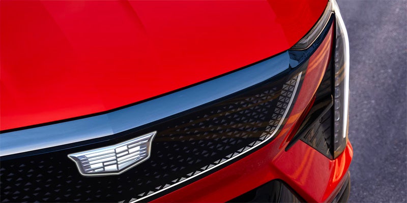 Close-up of the Cadillac OPTIQ front grille featuring the Cadillac crest, patterned mesh design, and sleek LED lighting detail.