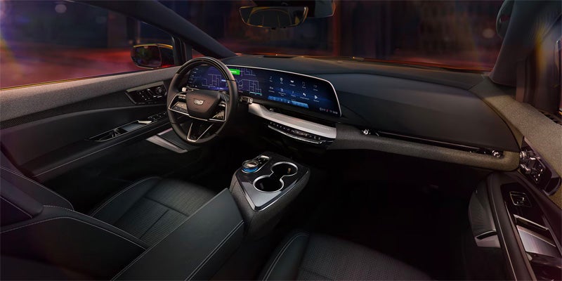 Wide interior view of the Cadillac OPTIQ showcasing the curved digital display, premium seating, ambient lighting, and modern center console design.