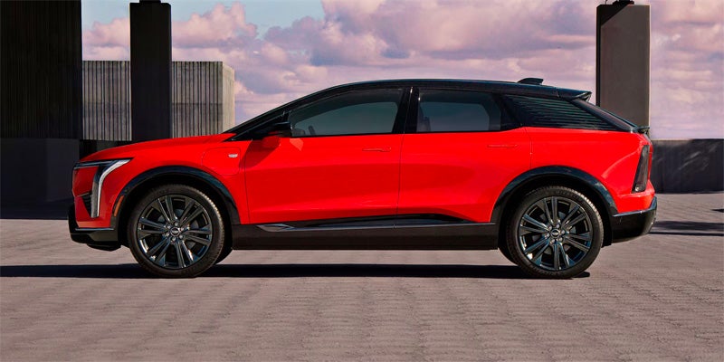 Side profile of the red 2026 Cadillac OPTIQ featuring a black contrast roof, sleek body lines, and large alloy wheels.