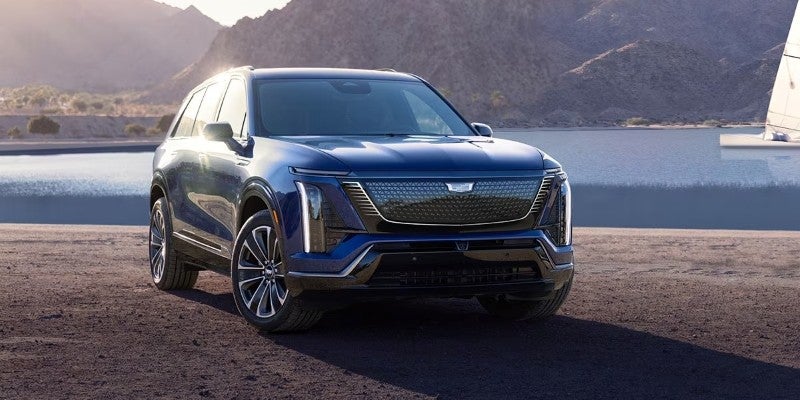 Front three-quarter view of the 2026 Cadillac VISTIQ electric SUV parked near a waterfront with mountains in the background.